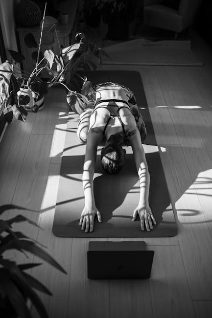 Woman in a white top performing a yoga pose on a wooden deck surrounded by tranquil water and greenery.